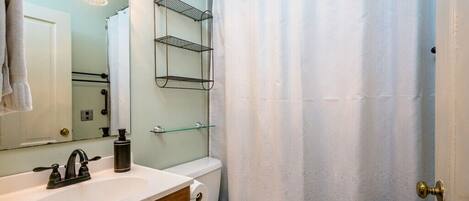 Un bagno con lavandino bianco, uno specchio, un portascopevoli, un water e una tenda da doccia.