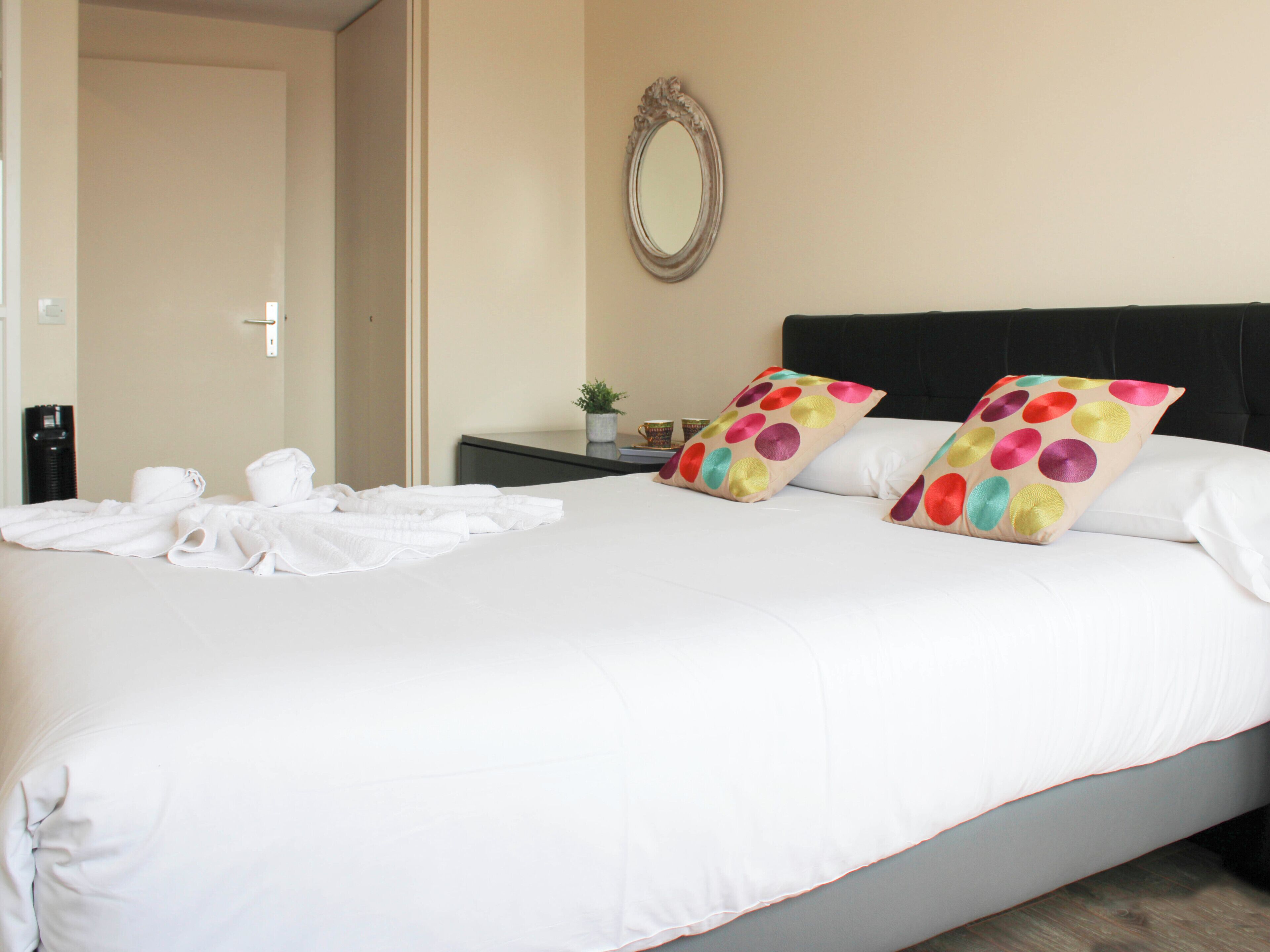Une chambre d’hôtel avec un lit, des oreillers, une table de chevet avec une plante, un miroir et un distributeur d’eau.