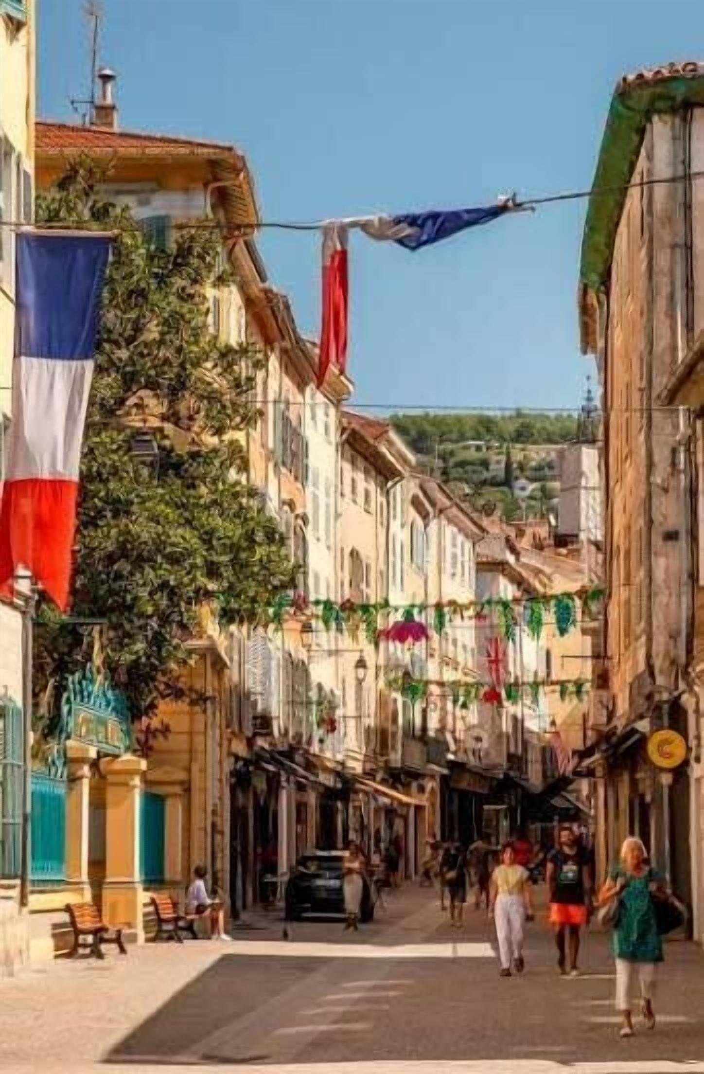 Una calle estrecha flanqueada por edificios, con banderas colgando y gente caminando.