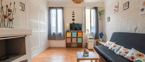 Una sala de estar con sofá, una mesa de centro, televisor, estantería y lámpara colgante.