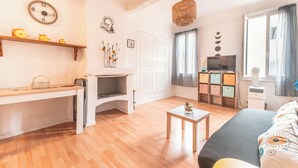 Una habitación con piso de madera, una cama, un televisor, un estante con adornos y un reloj de pared.