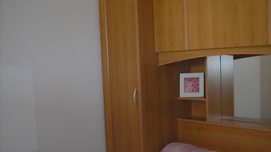 Quarto com uma cama, um guarda-roupa de madeira e uma pequena moldura com um quadro na parede.