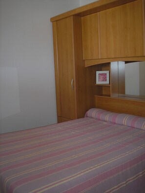 Ein Schlafzimmer mit einem Bett, einem Holzschrank und einem kleinen gerahmten Bild an der Wand.