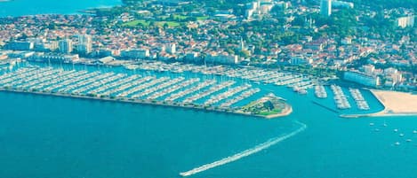 An aerial view of a coastal marina with numerous boats docked, surrounded by residential buildings and a sandy beach.