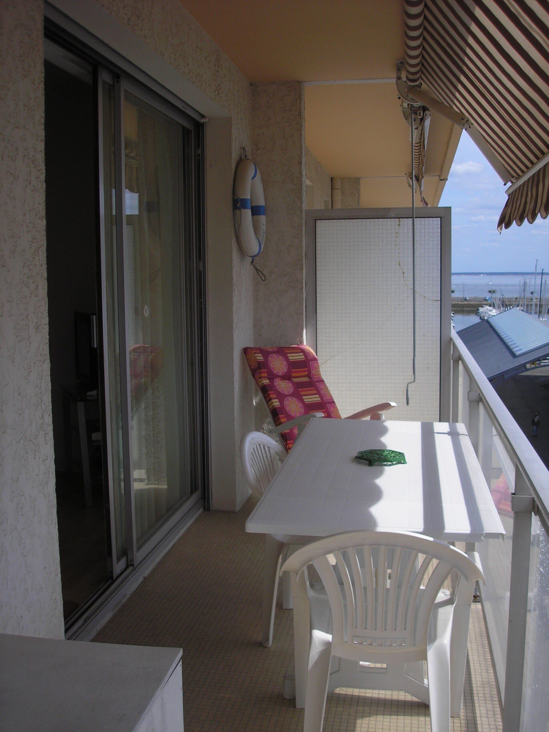 A balcony with a white table and chairs, a whiteboard, and a lifebuoy on the wall.