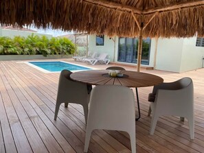 A wooden deck with a thatched roof, a pool, and lounge chairs. - Casa Eloi, Mambo Beach (Willemstad)