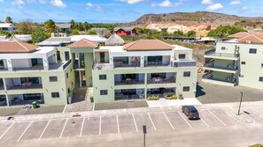 Un edificio residencial de varios pisos con balcones, un estacionamiento y un paisaje montañoso al fondo.