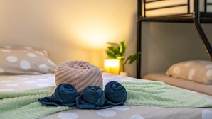 A neatly made bed with a green blanket and rolled towels, a bedside lamp, and a potted plant. - Felicidat Nobo, Mambo Beach (Willemstad)