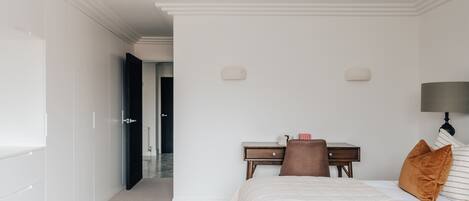 A hotel room with a bed, a desk, a chair, a nightstand, and a lamp.