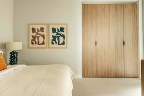 A bedroom with a bed, a nightstand with a lamp, and a wardrobe. - Stylish 2BD Residence in Prime Mayfair (London)