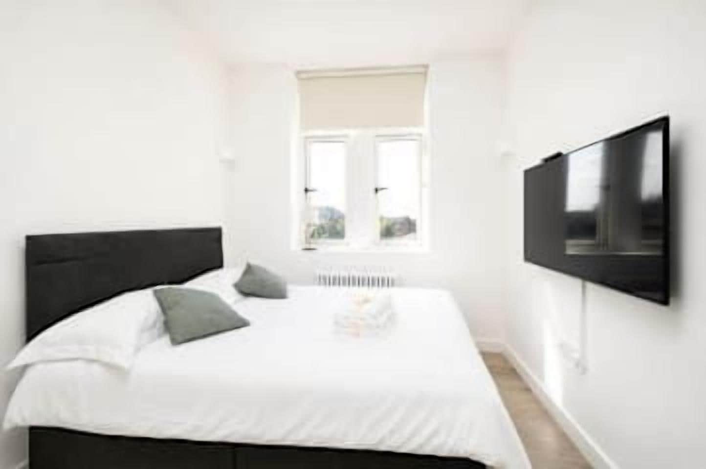 A bedroom with a bed, pillows, a TV, and a window.