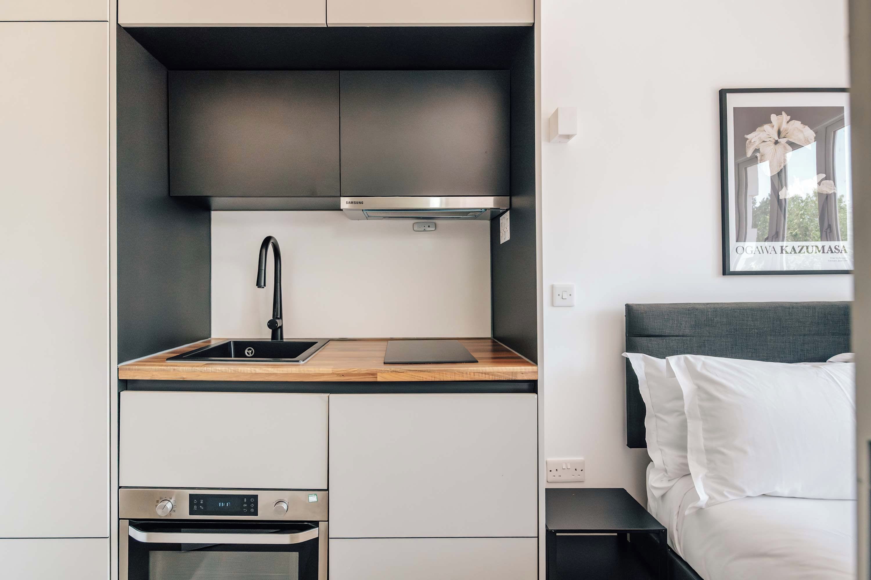Eine kompakte Küchenzeile mit modernem Design, inklusive Backofen aus Edelstahl, Spüle und kleiner Arbeitsfläche.