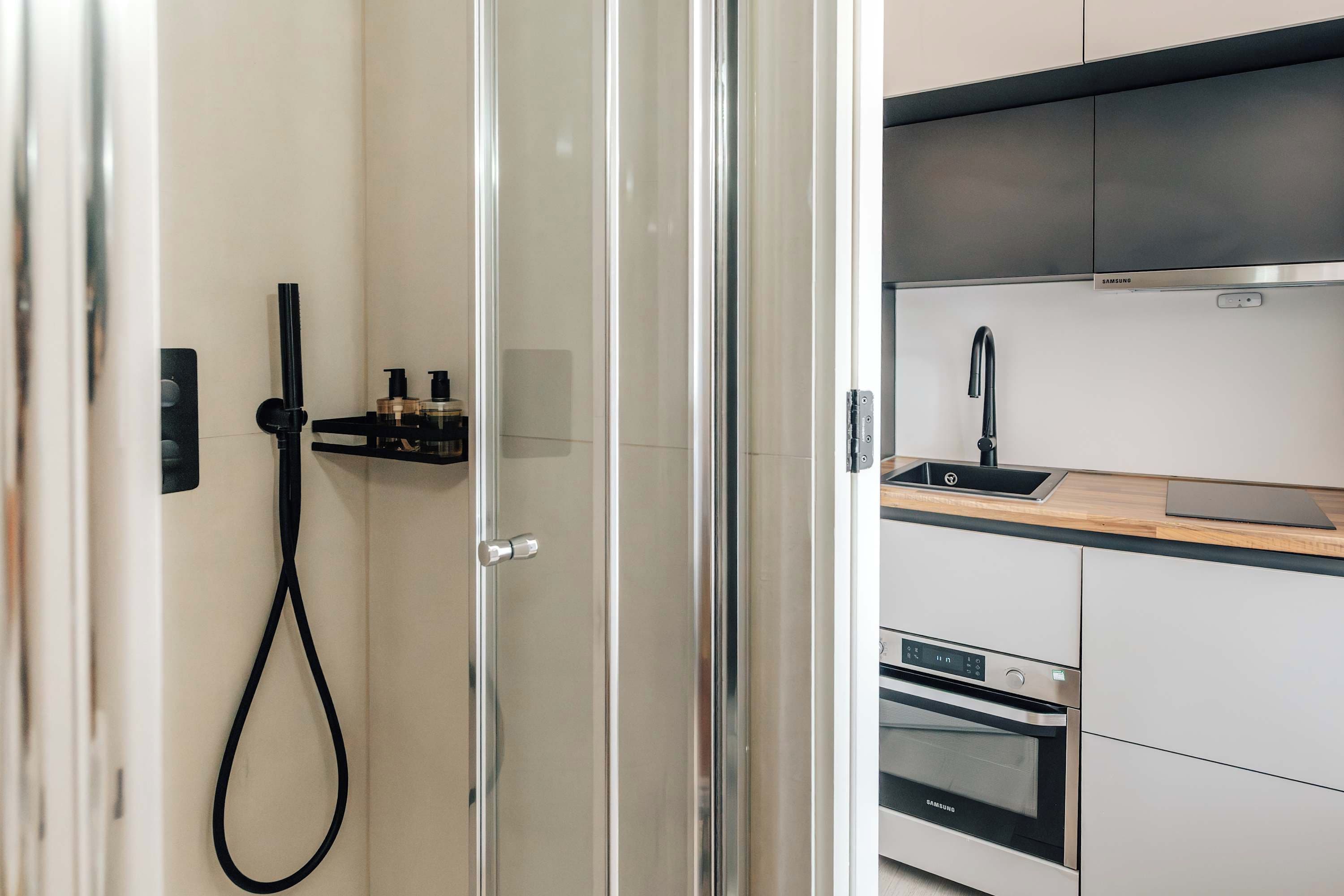 A modern kitchen with a built-in oven, a sink, and a glass shower enclosure.