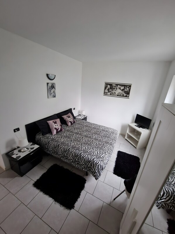 A bedroom with a zebra-patterned bed, a black rug, a white wall with a clock, and a TV stand.