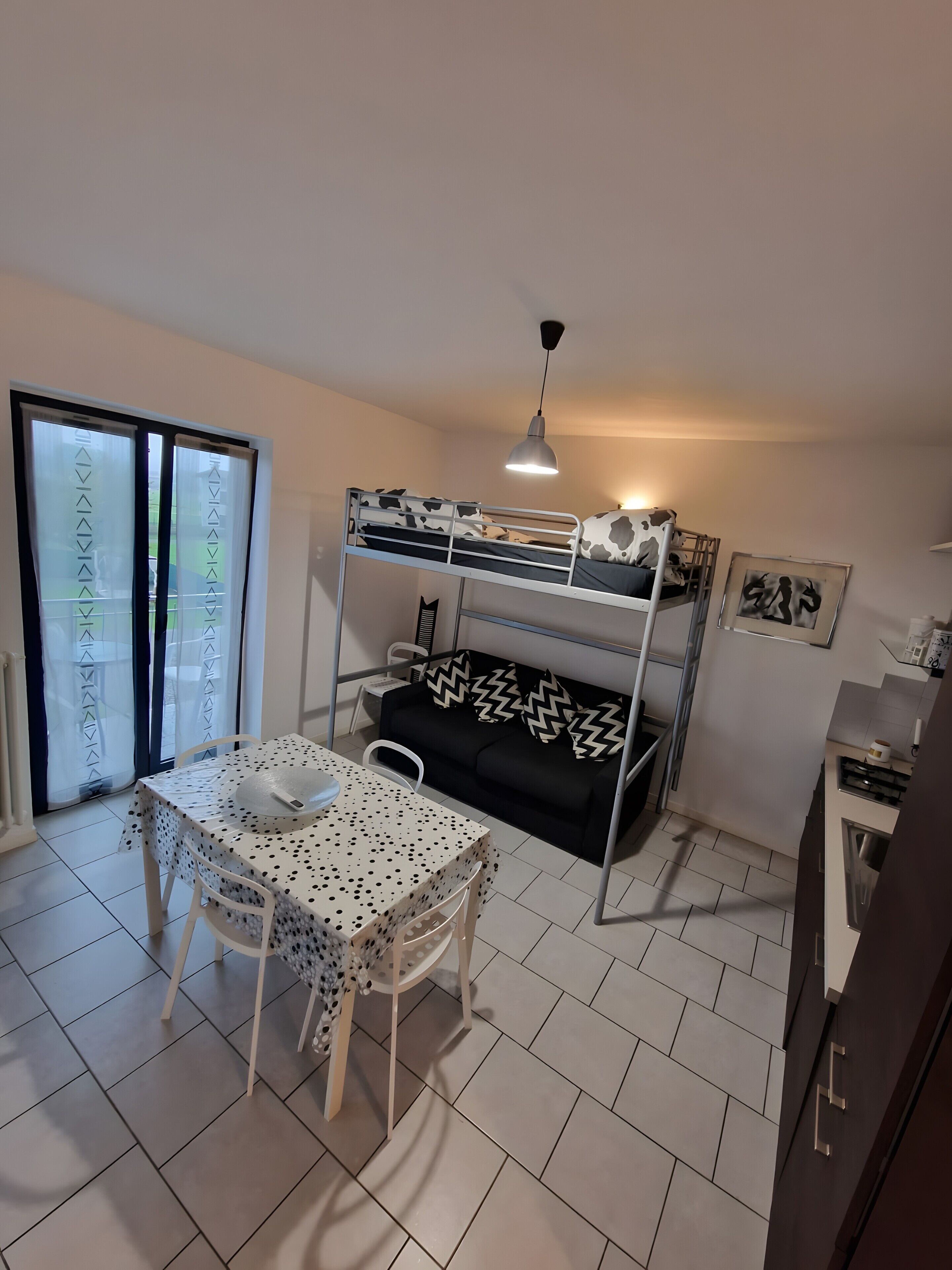 Habitación funcional con literas, una mesa de comedor con sillas, un espacio para la cocina y una puerta corrediza de vidrio.