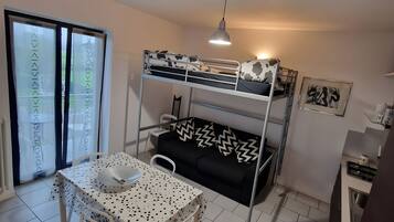Habitación funcional con literas, una mesa de comedor con sillas, un espacio para la cocina y una puerta corrediza de vidrio.