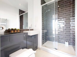 Een moderne badkamer met een douchecabine van glas, een donkere wastafel en een witte wasbak.