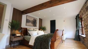 A bedroom with a wooden bed, a desk, a radiator, and a stone wall.