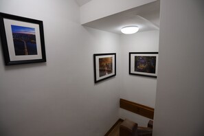 Een gang met drie ingelijste foto's aan de muur, een houten bankje en een plafondlamp.