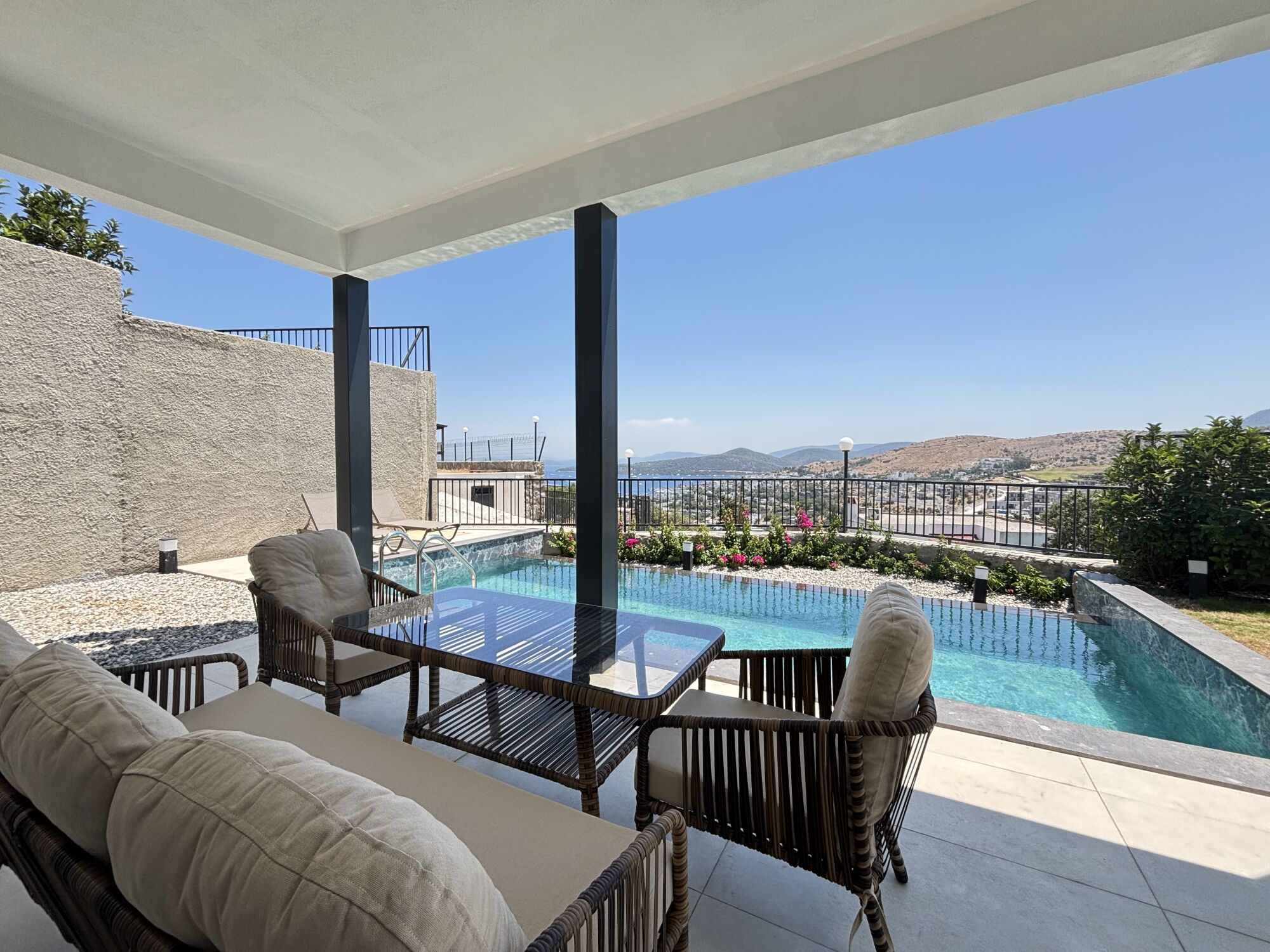 A poolside area with a view of the landscape, outdoor furniture, and a clear sky.