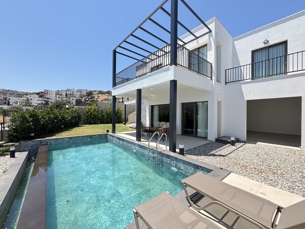 Une maison moderne à deux étages, dotée d’une piscine, de mobilier d’extérieur et offrant une vue sur le quartier environnant.