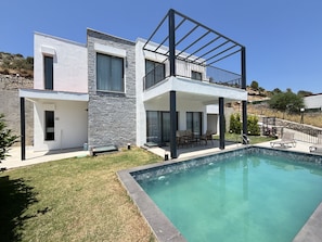 Ein modernes, zweistöckiges Haus mit Swimmingpool, Balkon und einer Stein-Fassade.