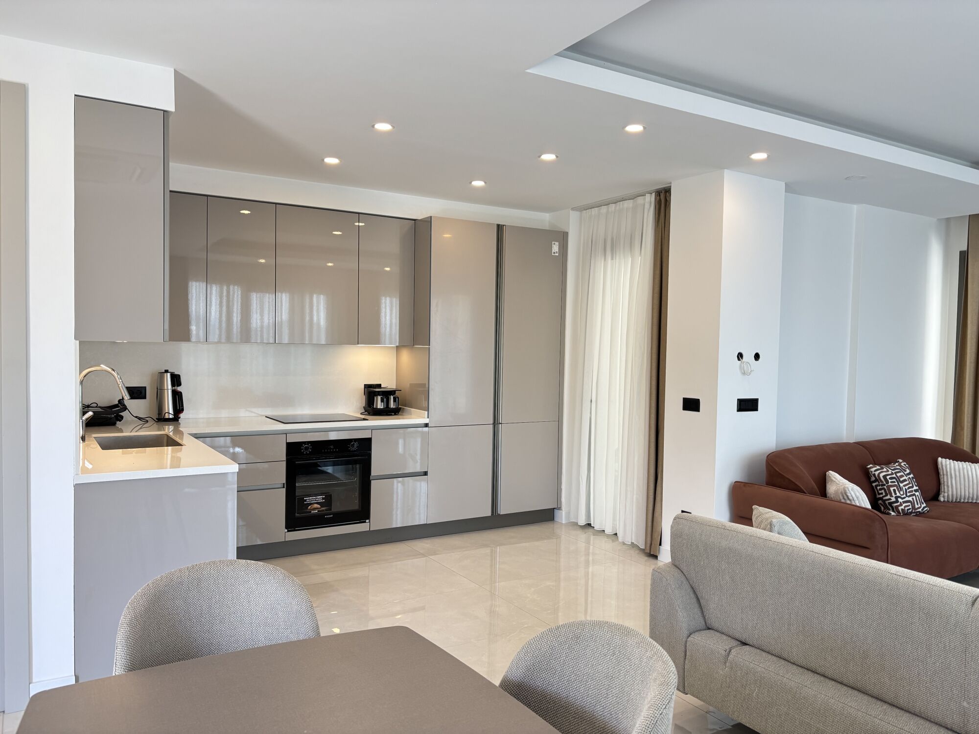 A modern kitchen with built-in appliances, a dining area with a table and chairs, and a living room with a sofa.