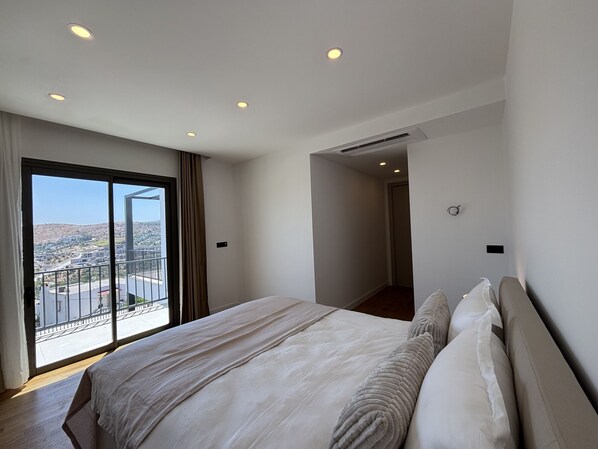 Ein Hotelzimmer mit einem großen Bett, Blick auf eine Stadtlandschaft vom Balkon und einem modernen Design.
