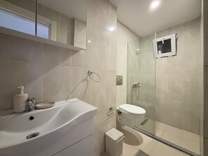 A modern bathroom with a white sink, toilet, and glass-enclosed shower. - Comfortable 2BR | Walk to Sultanahmet (Istanbul)