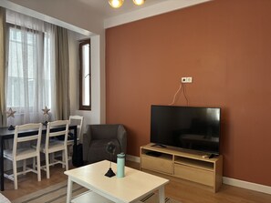 Una sala de estar con televisor, una mesa de comedor con sillas y una ventana con cortinas.