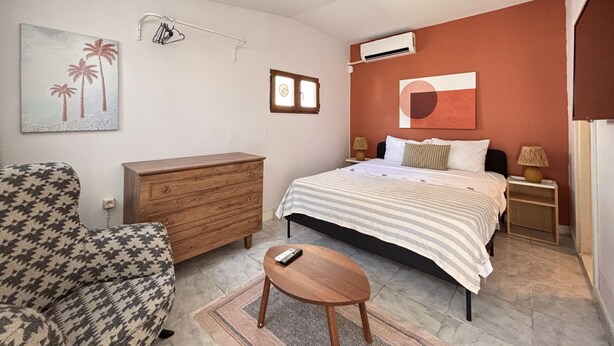 Ein Schlafzimmer mit einem Bett, einem hölzernen Schminktisch, einem Sessel, einer Klimaanlage und einem Bild an der Wand.