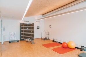 Un gimnasio con equipo de ejercicio, suelo de madera y colchonetas rojas.