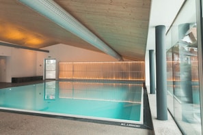 Piscina interior con vista despejada de la estructura del techo y una pared de vidrio que refleja el exterior.