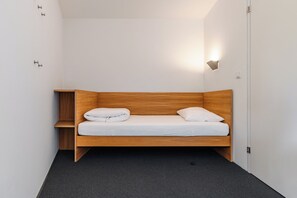 Un dormitorio pequeño y moderno con una cama de madera, una mesita de noche y una lámpara de pared.