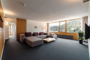 A modern living room with a sectional sofa, a coffee table, and a large window offering a view of a forested mountain.