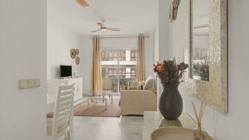 A modern living room with a glass coffee table, a white sofa, a large mirror, and a ceiling fan.