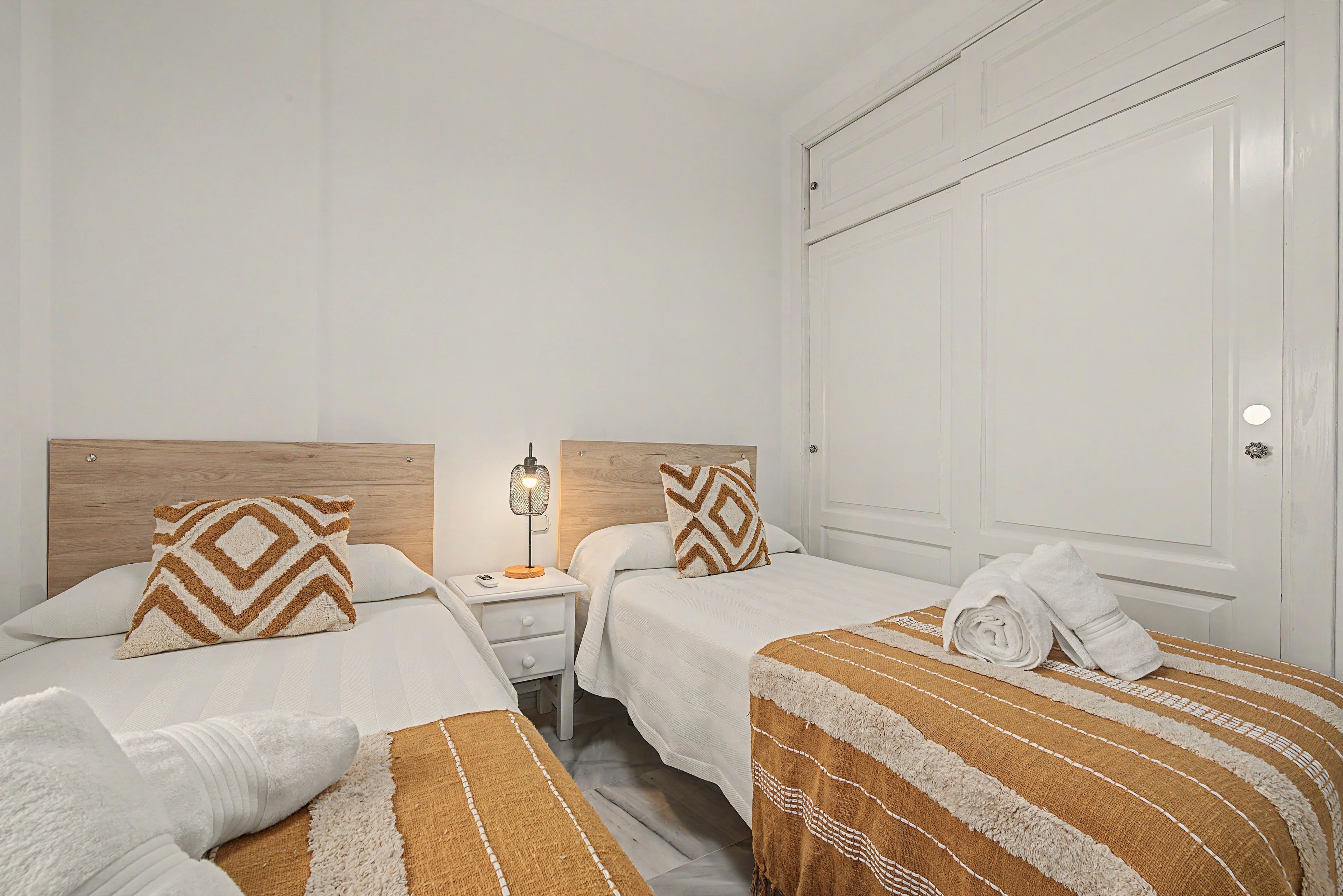 A hotel room with two beds, a nightstand with a lamp, and a large wardrobe.
