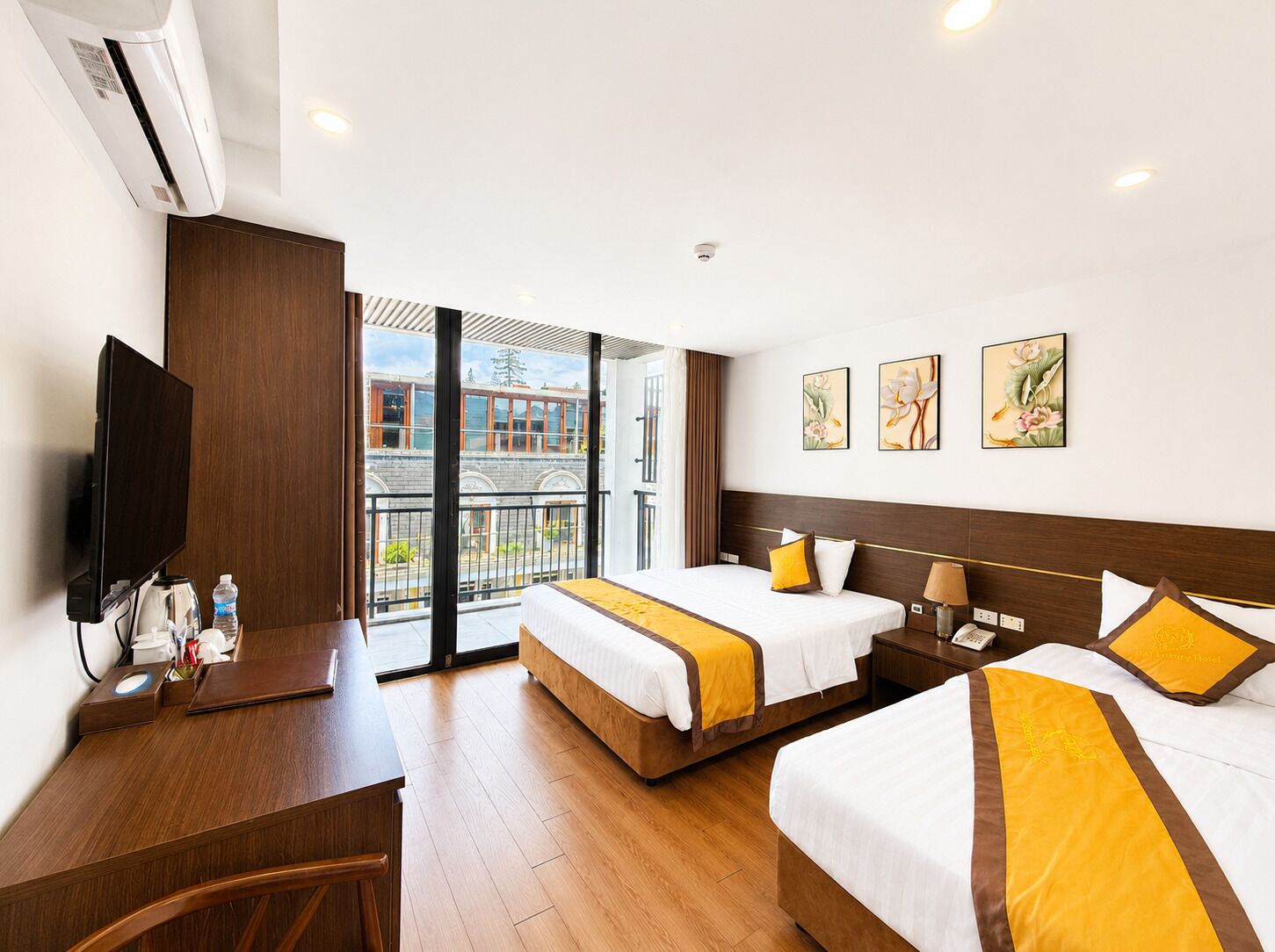A hotel room with two beds, a desk, a flat-screen TV, and artwork on the wall.