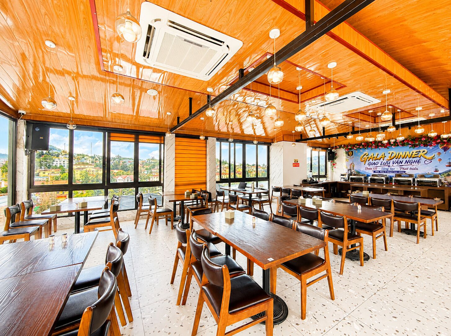 A spacious dining area with multiple tables and chairs, large windows offering a view of the city, and a banner advertising a gala dinner.