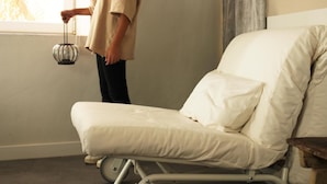 A hospital bed with a pillow and a person standing beside it, holding a lamp.