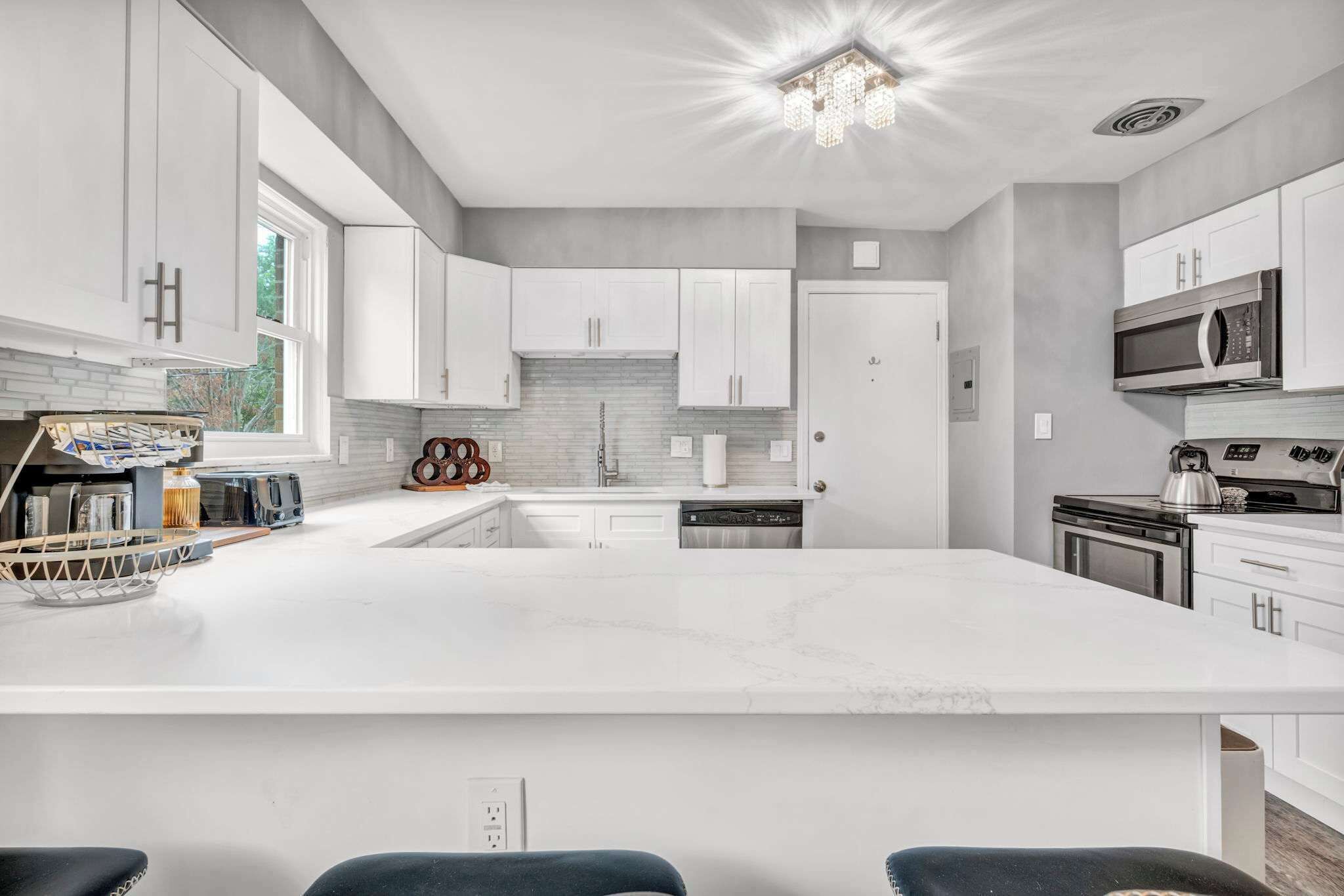 Een moderne keuken met witte kasten, een groot eiland, roestvrijstalen apparatuur en een kroonluchter.