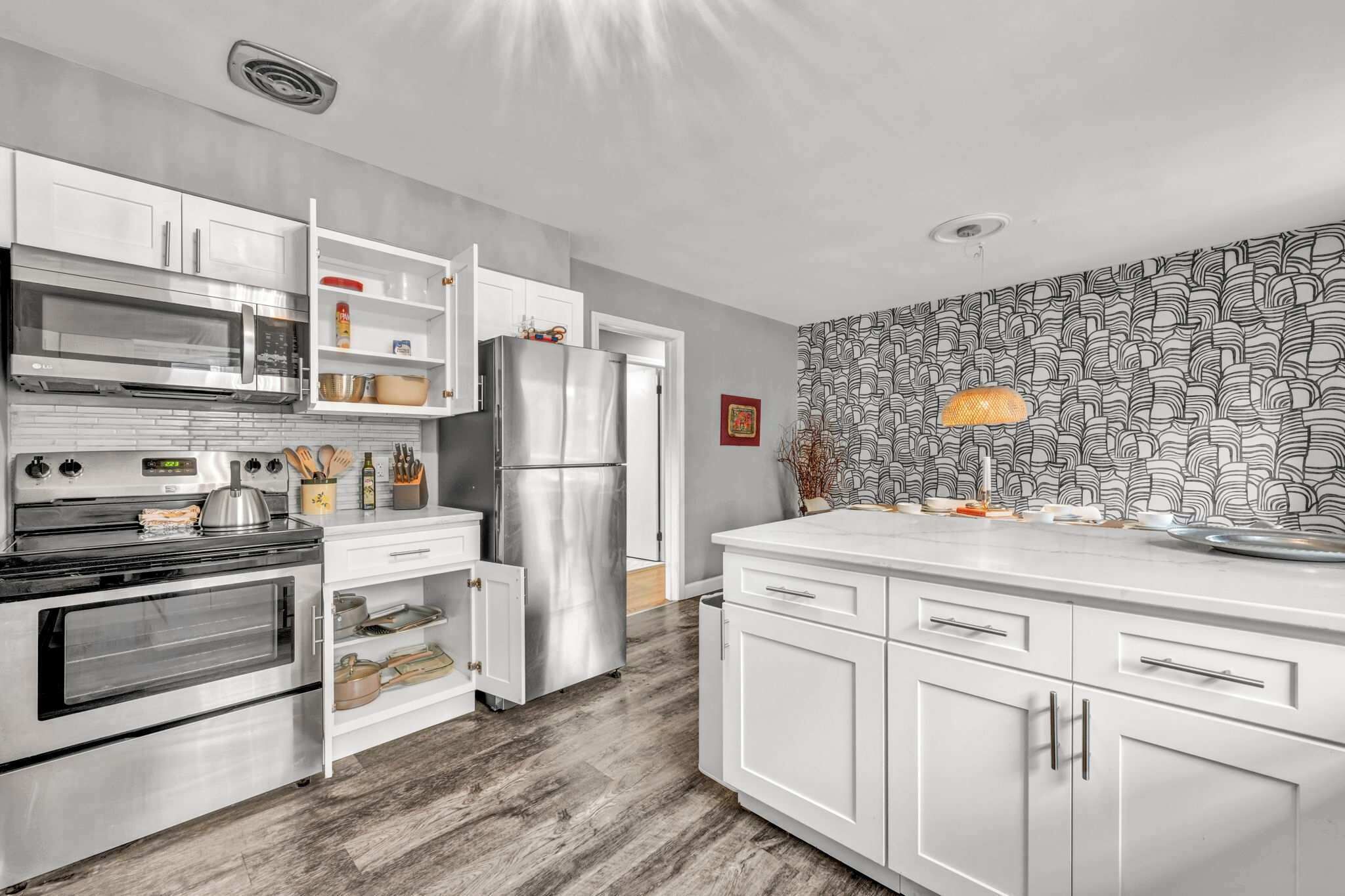 A modern kitchen with white cabinetry, stainless steel appliances, and a patterned wallpaper.
