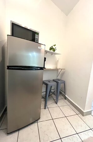 A compact kitchen with a stainless steel refrigerator, a microwave, and a small stool. - Beach, Cafés & La Placita on Foot / Condado (San Juan)