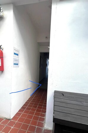 A corridor with a tiled floor leading to a door, a fire extinguisher on the left, and directional signs on the wall. - Beach, Cafés & La Placita on Foot / Condado (San Juan)