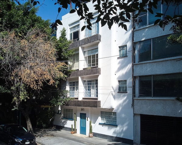 Un edificio bianco con una porta blu, diverse finestre e un cartello con il numero civico visibile.