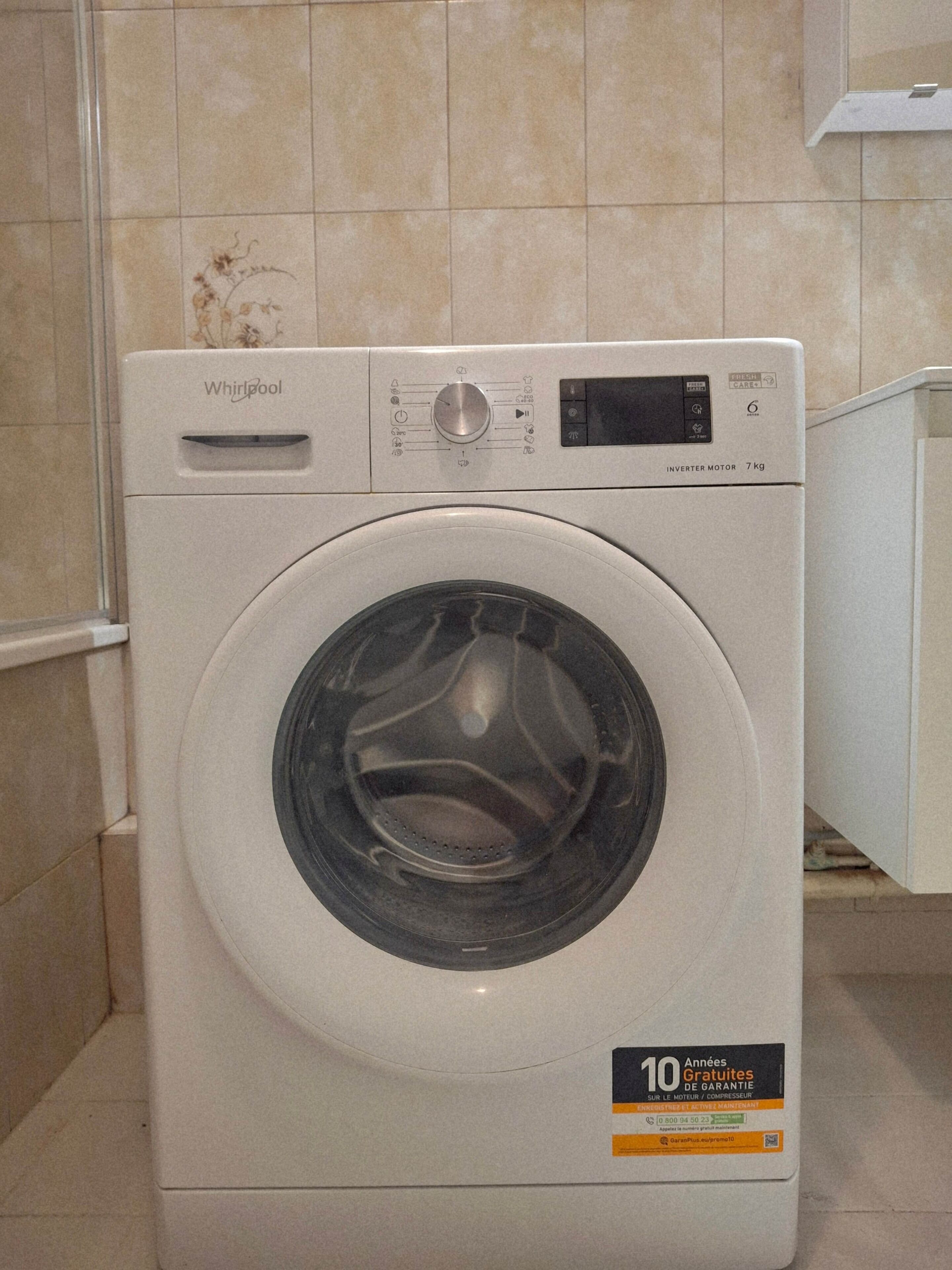 Une machine à laver Whirlpool dotée d’un écran numérique, d’un panneau de commande et d’un autocollant indiquant une garantie de 10 ans.