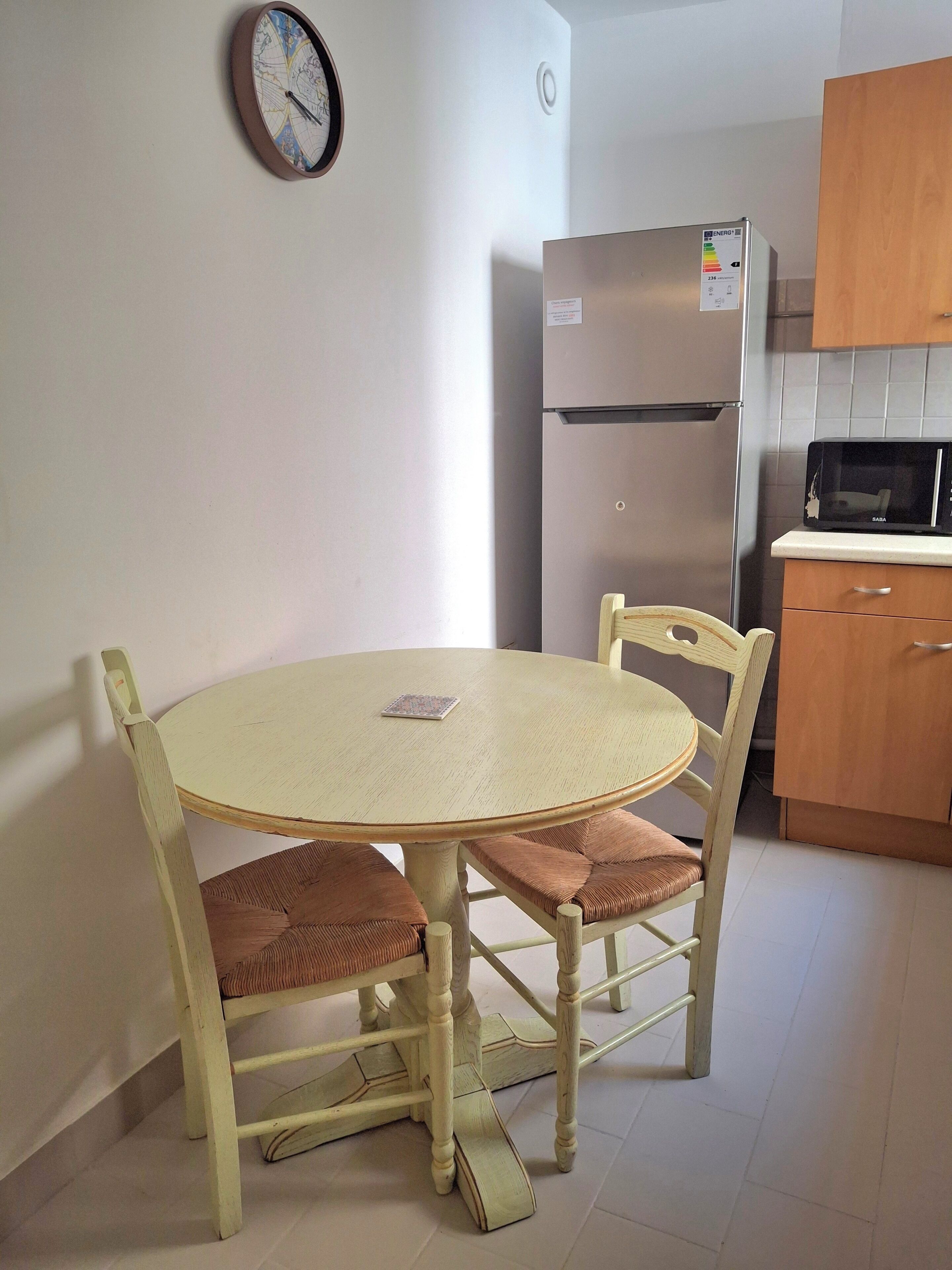 Een kleine keuken met een ronde tafel, stoelen, een koelkast en een magnetron.