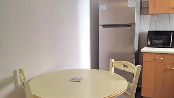 Een kleine keuken met een ronde tafel, stoelen, een koelkast en een magnetron.