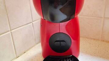 Eine rote und schwarze Kaffeemaschine mit einem schwarzen Auffangbehälter, auf dem 'KRUPS' steht, auf einer Arbeitsplatte.