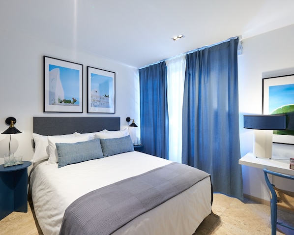 Ein modernes Hotelzimmer mit einem großen Bett, zwei gerahmten Bildern, einem Schreibtisch und einem Sessel.